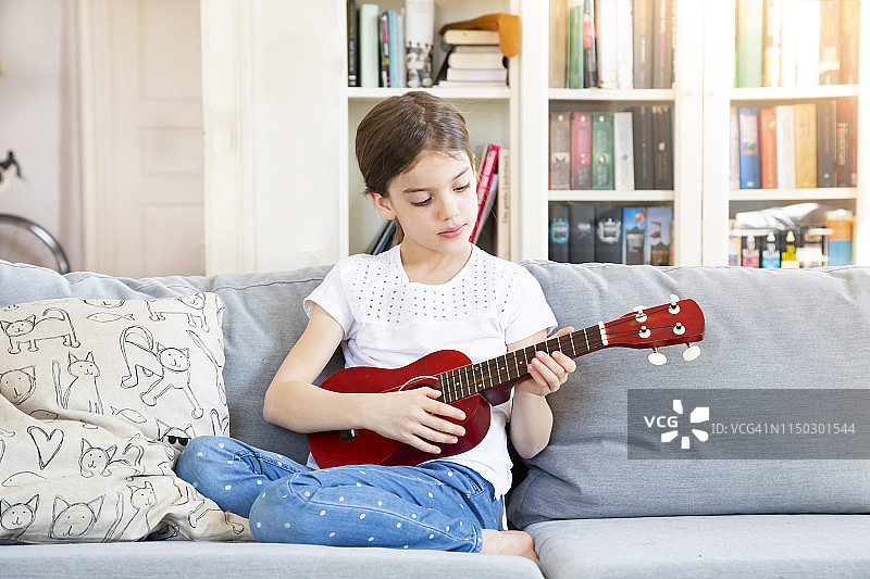 一个女孩坐在家里的沙发上弹奏四弦琴图片素材