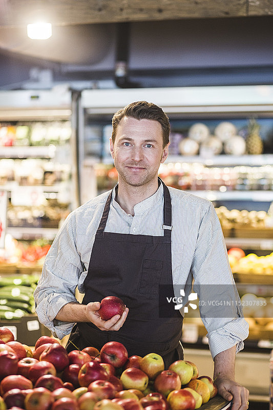 自信微笑的企业家手拿苹果站在超市的肖像图片素材