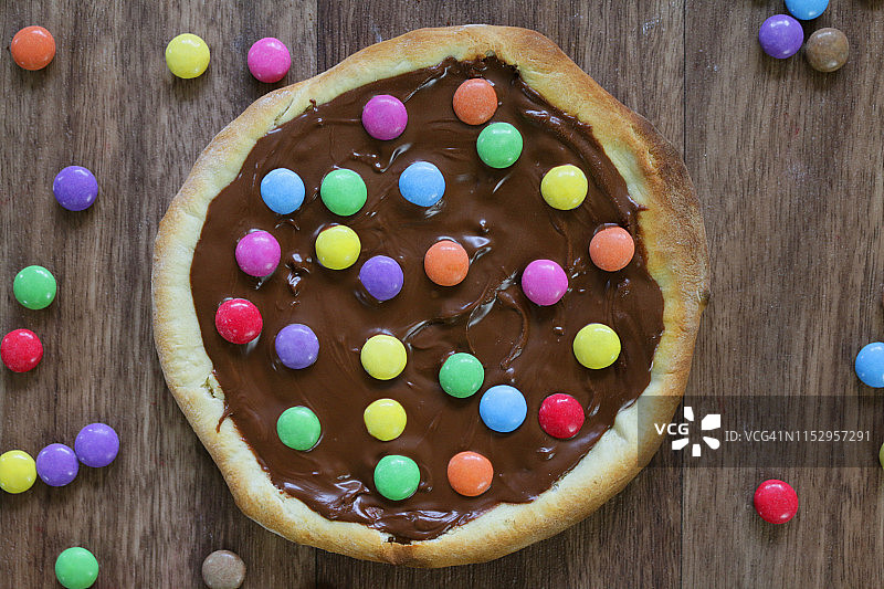 图片自制的巧克力披萨与多色糖果糖果和糖霜糖，烤披萨皮充满榛子巧克力涂抹儿童，顶部是脆糖涂层彩虹smarties巧克力糖果，吃布丁甜点图片素材