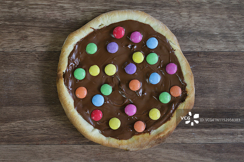 图片自制的巧克力披萨与五彩糖果糖果和糖霜糖，烤披萨皮充满榛子巧克力涂抹儿童，顶部是脆糖涂彩虹smarties巧克力糖果，吃布丁甜点图片素材