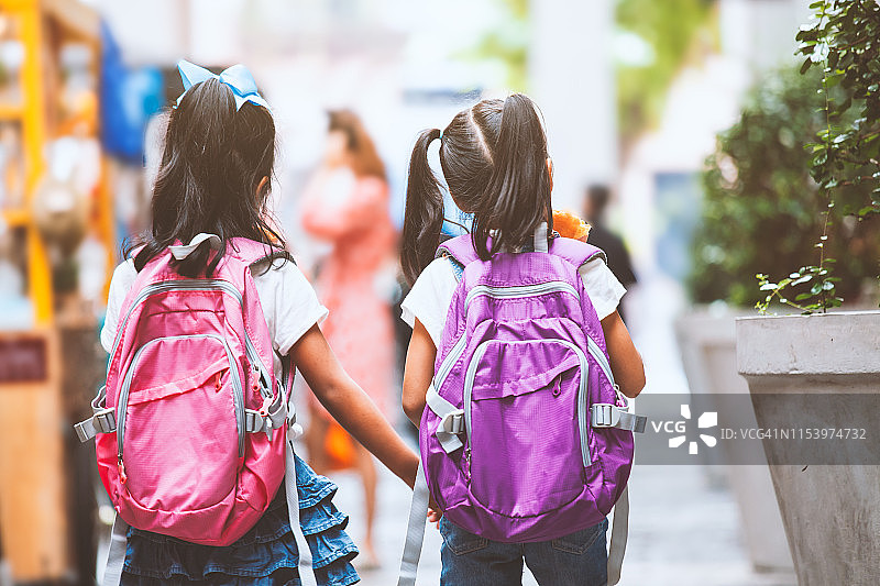 两个可爱的亚洲小女孩手拿书包，一起走在学校里图片素材