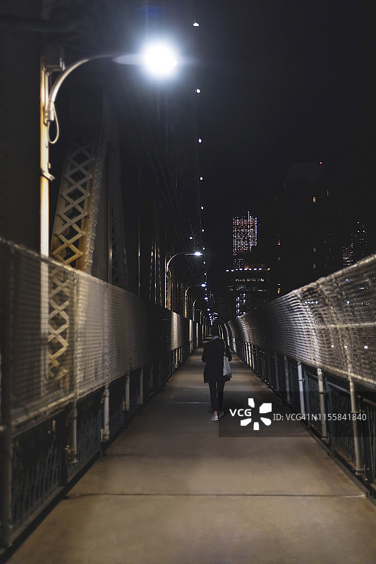年轻女子在夜里走过桥。图片素材