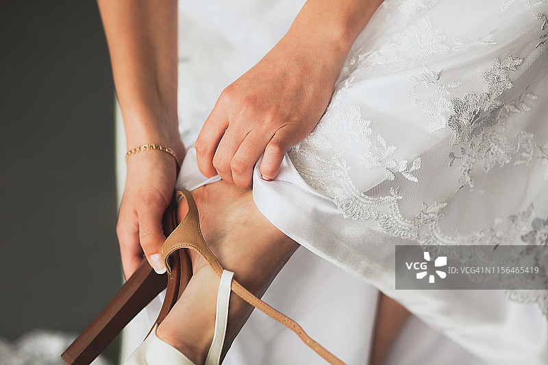 新娘，女孩或年轻女子在美丽优雅的现代时尚的婚纱穿上一条腿轻皮革时尚高跟鞋，特写。婚礼当天还是早上。图片素材