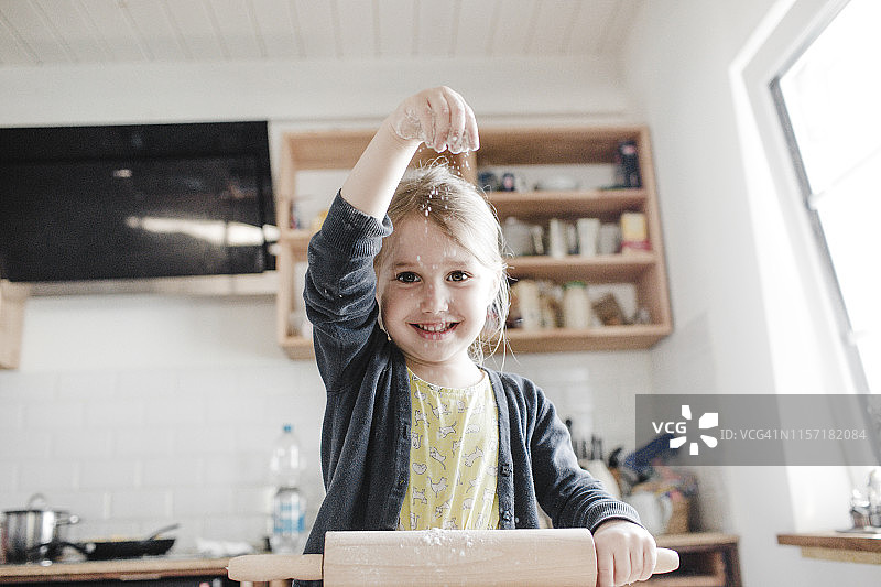 一个微笑的小女孩在厨房擀面团的肖像图片素材