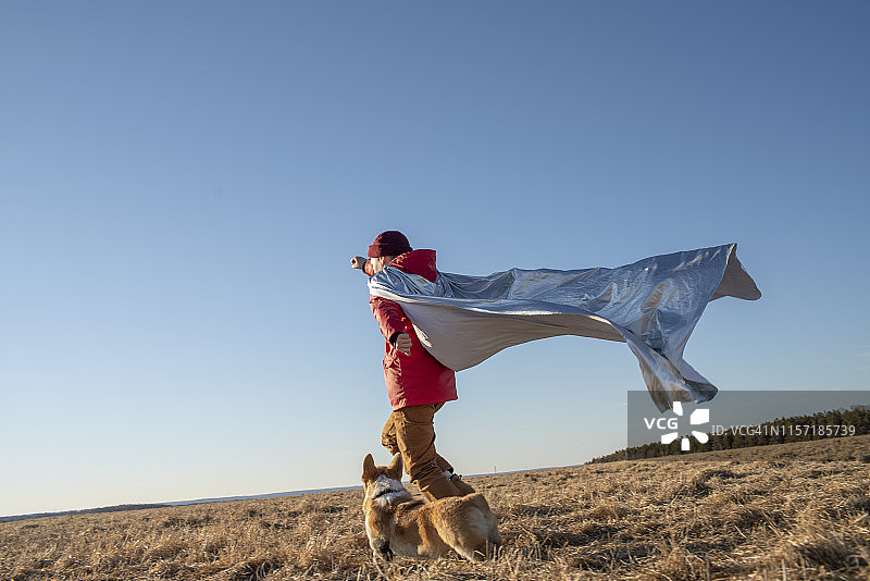 男孩打扮成超级英雄和狗在草原上奔跑图片素材