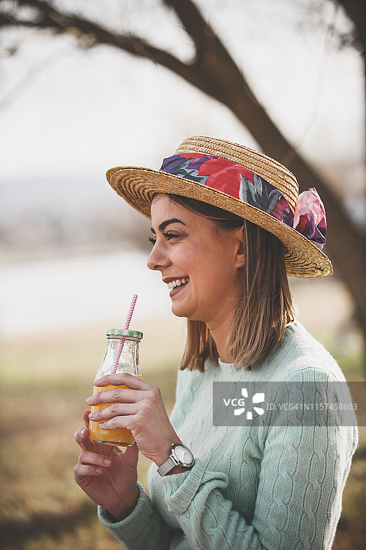 戴着帽子在户外喝果汁的漂亮女人图片素材
