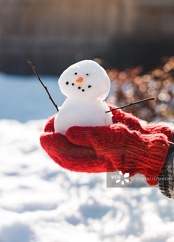 在红色羊毛手套的手近举一个小雪人。图片素材
