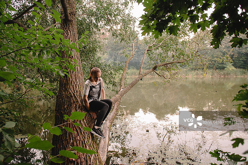 一个年轻女子坐在森林里湖面上的树上图片素材