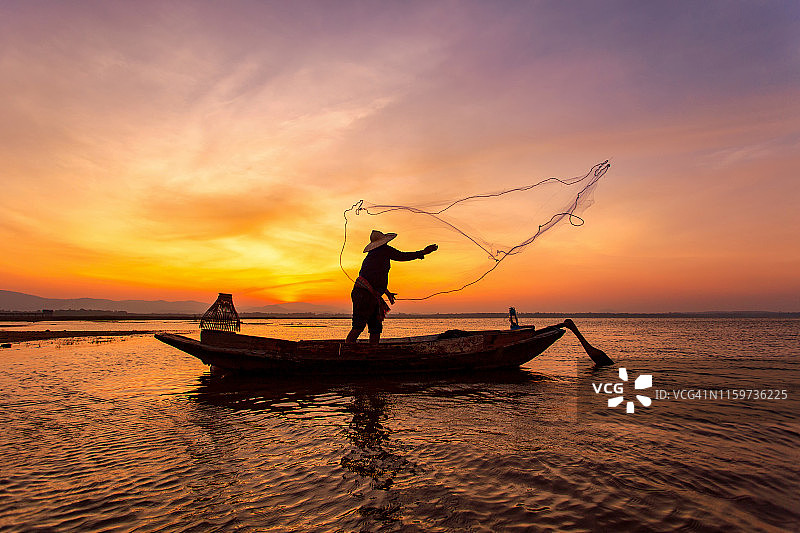 在美丽的日落背景下，渔民在湖上的船的剪影图片素材