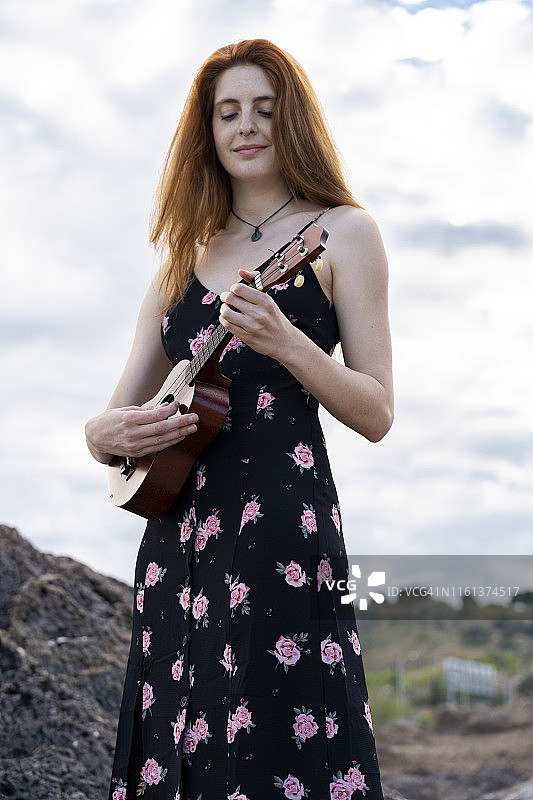 肖像微笑红发年轻女子穿着夏季连衣裙与花设计玩尤克里里图片素材