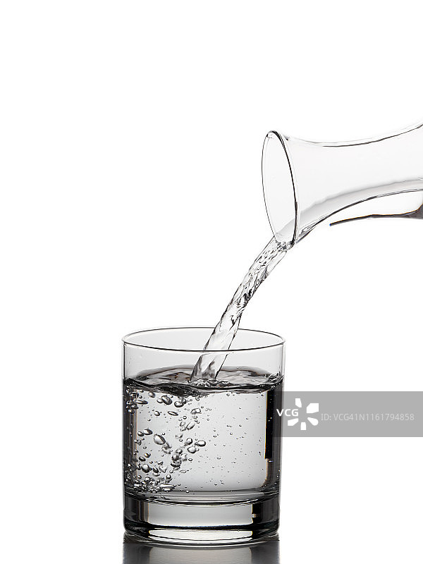 白色背景上的玻璃瓶水装满了一个饮用玻璃杯。图片素材