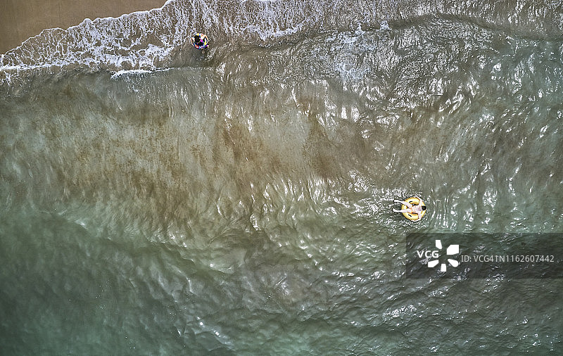 鸟瞰图上的小男孩游泳在黄色游泳环在透明的绿松石海在帕塔拉图片素材