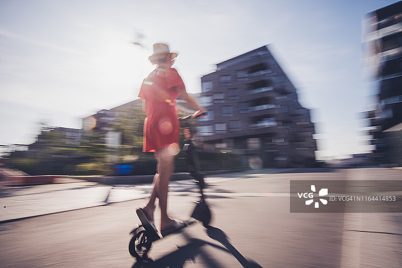 年轻女子骑着电动车在阳光明媚的日子里，模糊的运动。图片素材