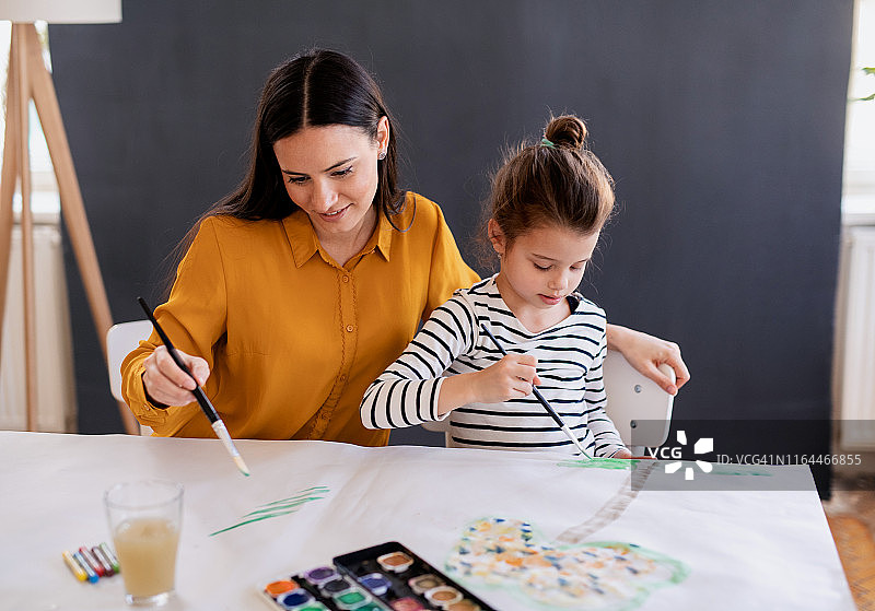 母亲和女儿坐在家里的桌子旁，画画。图片素材