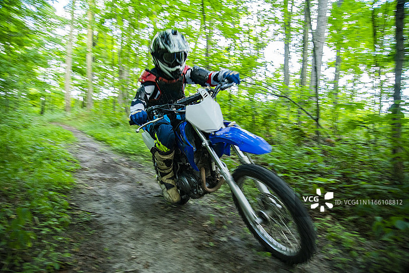年轻的摩托车手骑着摩托车在树林里。图片素材