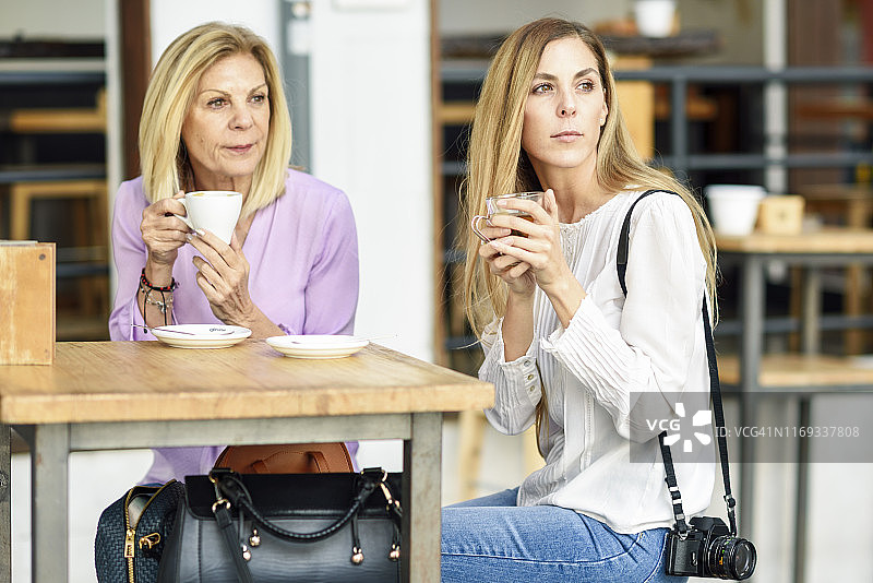 成熟的女人和她的女儿喝咖啡和茶坐在户外的桌子在一个咖啡馆图片素材