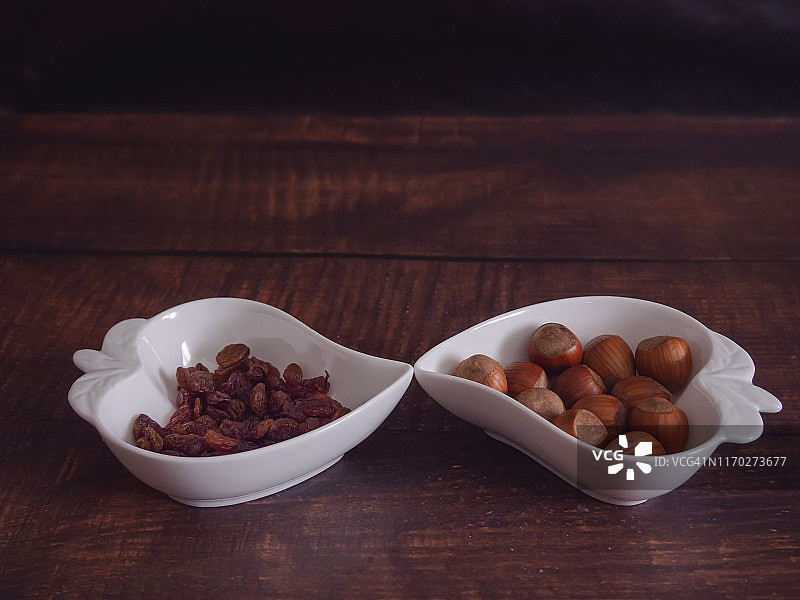 秋天的水果:一堆榛果和葡萄干，放在一个旧木桌上的心形瓷碗里图片素材
