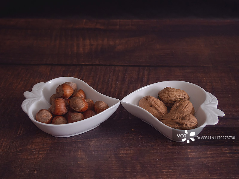 秋果:两组核桃和榛子，放在一个旧木桌上的心形瓷碗里图片素材
