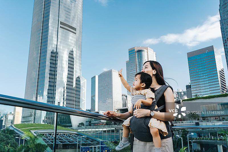 年轻的亚洲母亲和可爱的小女儿俯瞰香港的城市景观，在城市露台在金融区的城市风景图片素材