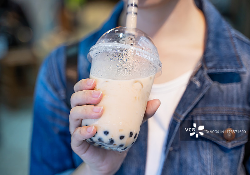 身着牛仔夹克的年轻女孩正在台湾夜市用玻璃吸管喝着红糖味的木薯珍珠奶茶图片素材