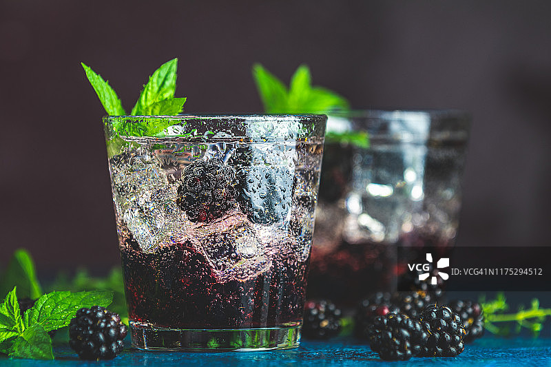 寒冷的夏季浆果饮料与黑莓。清爽的夏季饮料，糖浆，黑莓和冰在深蓝色的混凝土背景图片素材