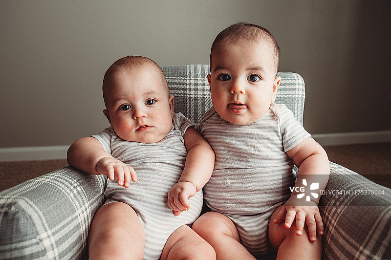 7个月大的男性异卵双胞胎坐在格子摇椅上，穿着一件灰色和白色连体衣图片素材