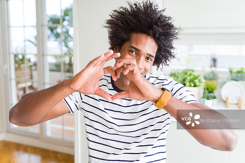 非裔美国男子穿着条纹t恤在爱中显示心形符号和形状的手。浪漫的概念。图片素材