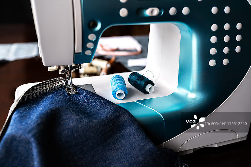 有牛仔布和缝纫线的缝纫机，特写。一台有蓝布的缝纫机的一部分。图片素材