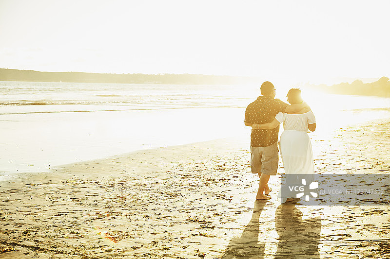 日落时分，一对成熟的情侣在海滩上手挽手散步图片素材