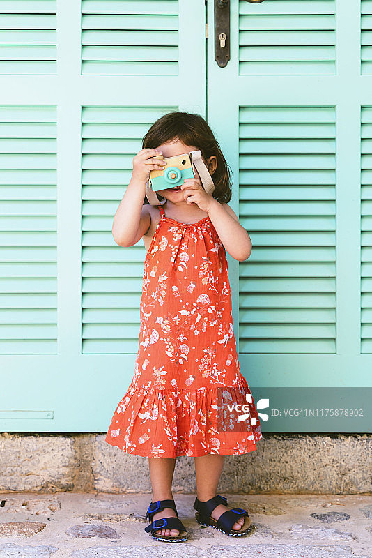 小女孩穿着红色的花裙子，玩着木制的玩具相机图片素材