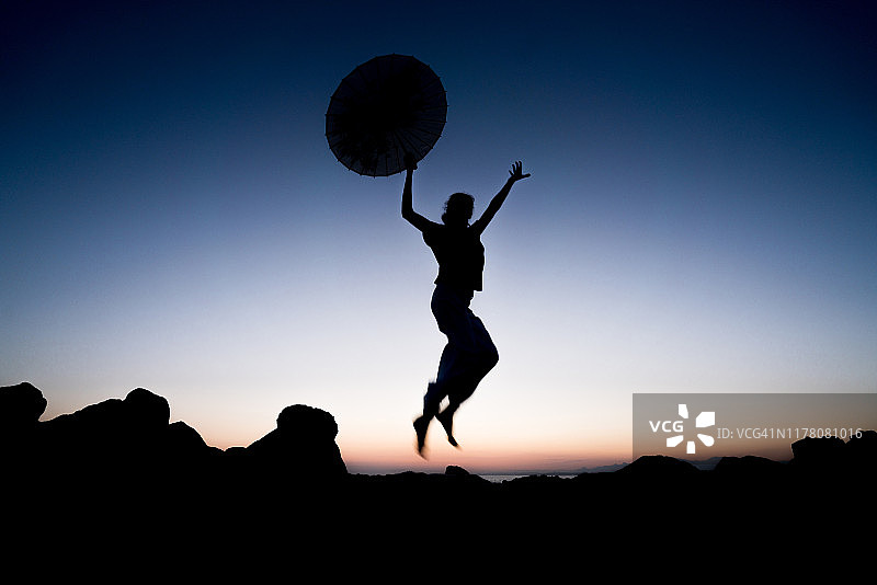 剪影的年轻女子跳上岩石与日本伞图片素材