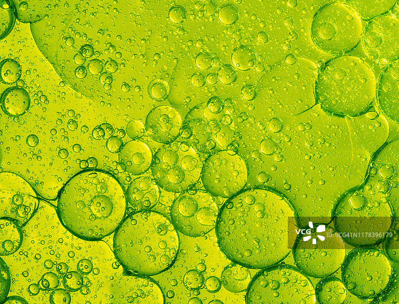 由绿色液体背景上的气泡和水滴构成的抽象形状和纹理的完整框架。图片素材