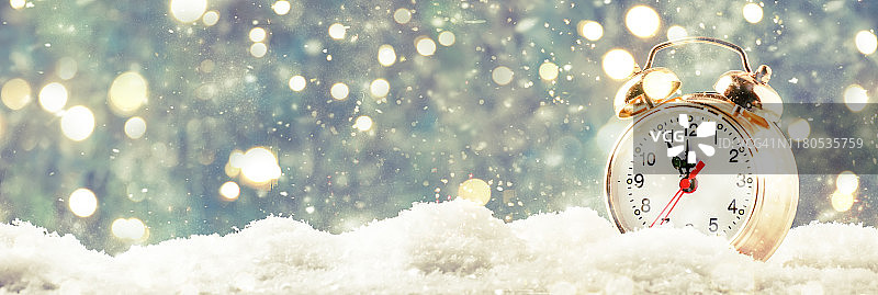 圣诞节或新年背景与金色的闹钟在雪堆上的蓝色背景与节日灯数圣诞倒数到午夜前的最后时刻。图片素材