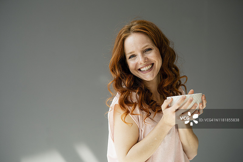 灰色背景下，一个快乐的红发女人拿着碗麦片图片素材