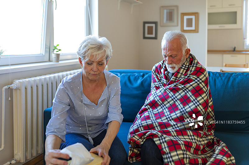 当她们坐在客厅的沙发上时，一位老妇人帮助生病的丈夫。她给他吃药，照顾他。图片素材
