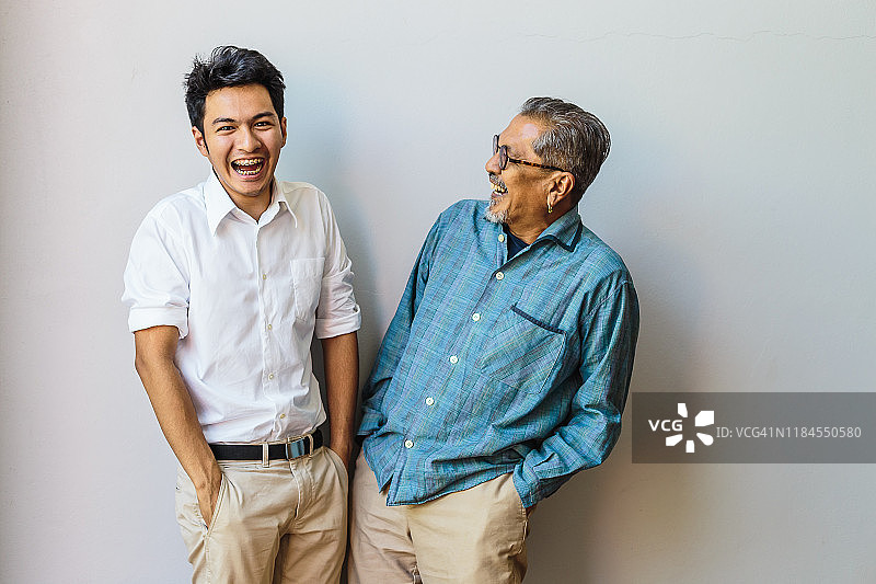 亚洲老父亲和他的成年儿子一起玩耍的肖像，站在灰色的背景上图片素材