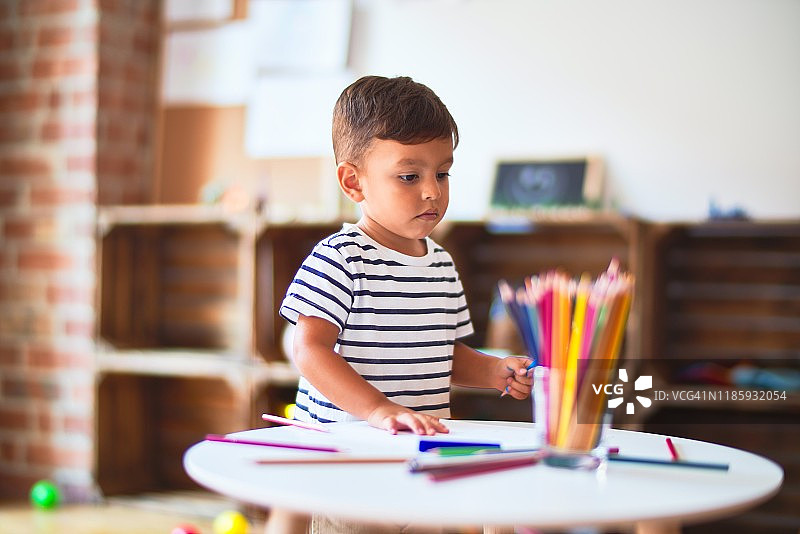 美丽的蹒跚学步的男孩在幼儿园用彩色铅笔画可爱的画图片素材