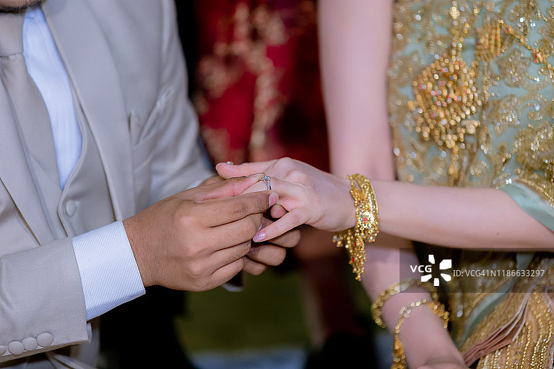结婚戒指。他给她戴上了结婚戒指。新郎把戒指戴在新娘身上。泰式婚礼和泰式婚礼装饰。把戒指戴在新娘的手指上。图片素材