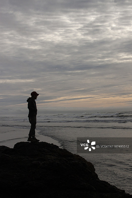 一个人的剪影站在悬崖上望着大海。图片素材