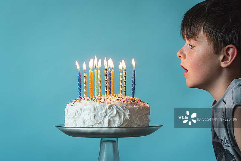 男孩准备在蓝色背景下吹灭生日蛋糕上的蜡烛。图片素材