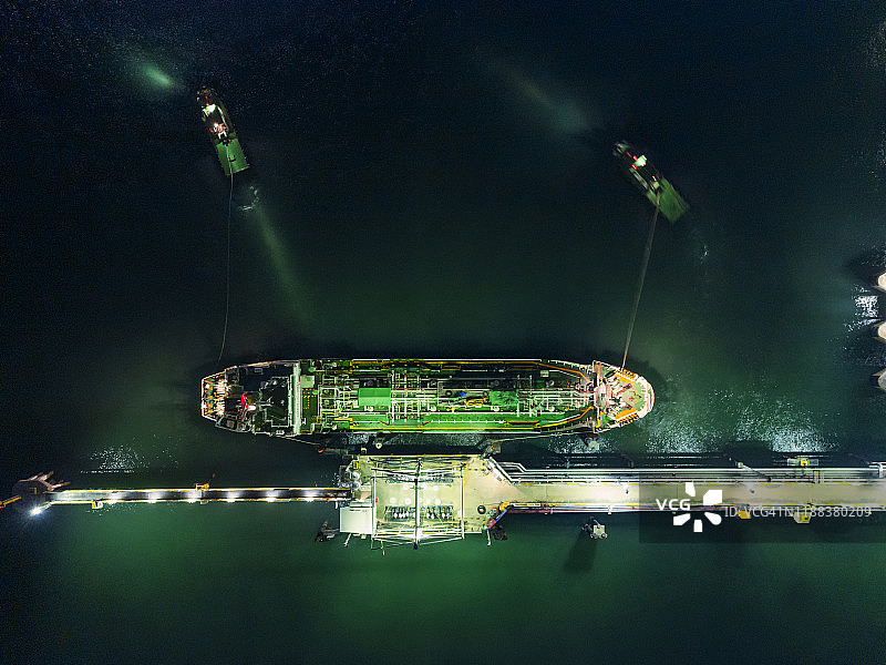 航拍俯视图拖船拖着油轮从装货码头夜间运输。图片素材