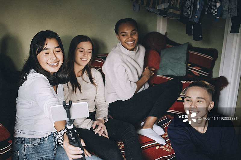 微笑的少女与朋友在单脚架上自拍，而享受在家里图片素材