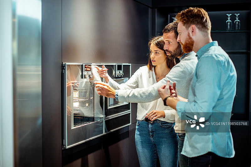 在厨房设备商店里，售货员向顾客解释新型电烤箱的特点图片素材
