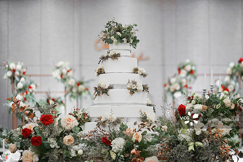 婚礼蛋糕。婚礼上的纯白色婚礼蛋糕。装饰有红玫瑰、康乃馨等鲜花。图片素材