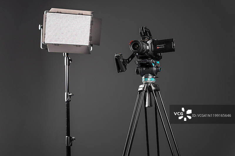 专业影院摄像机在一个摄像机三脚架和一个照明LED面板在黑色背景图片素材