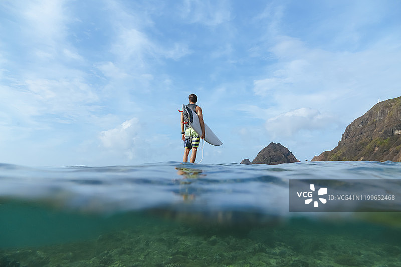 印度尼西亚松巴哇岛，冲浪者举着他的冲浪板，站在石头上图片素材