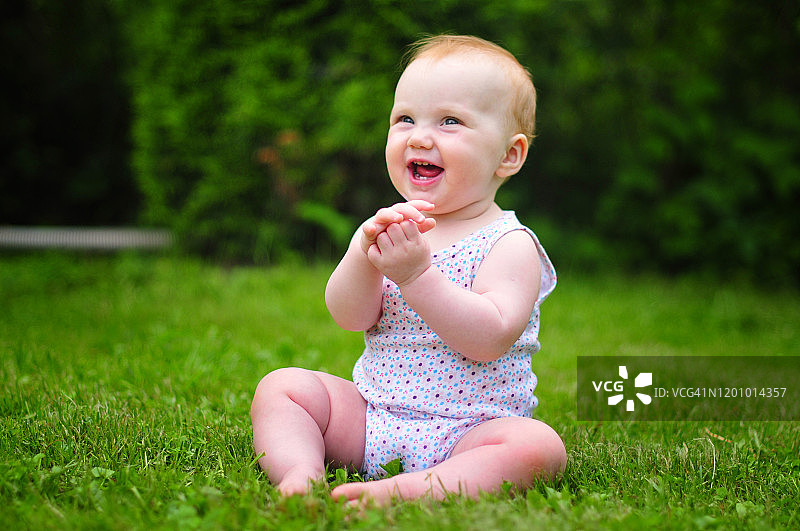 婴儿坐在绿色的草地上，拍着手。阳光明媚的夏日。快乐的孩子在花园里玩耍图片素材