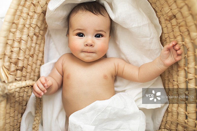 可爱的微笑美丽的小女孩躺在复古的婴儿柳条床。图片素材