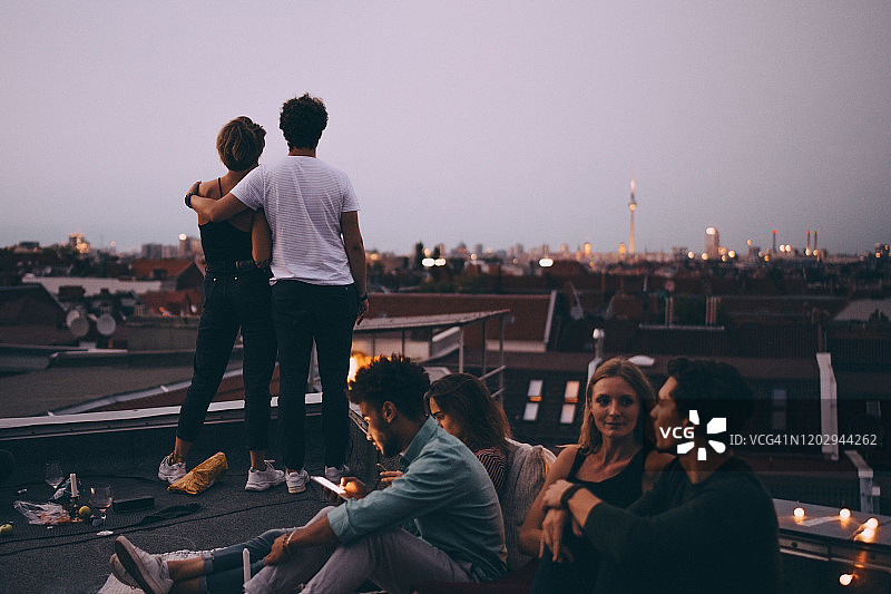 情侣看城市，而朋友放松在露台上在屋顶派对图片素材