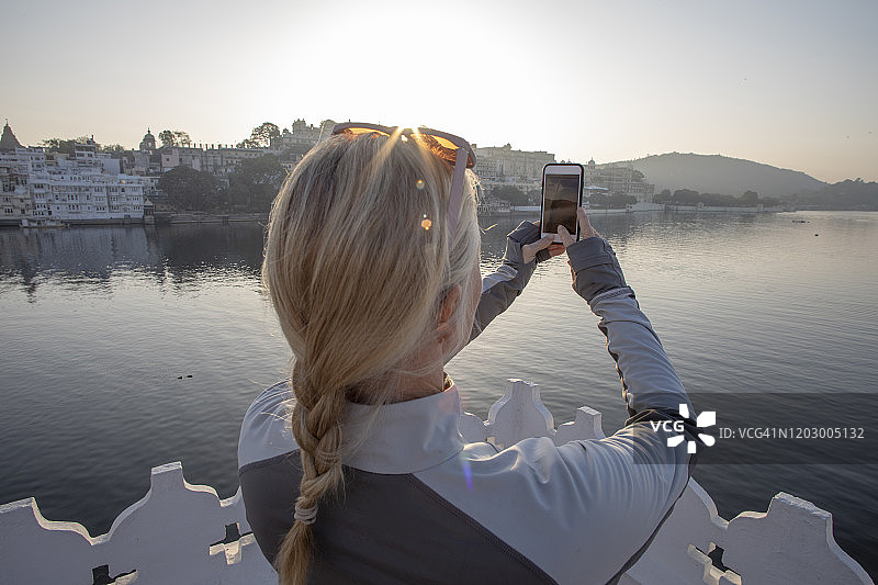 成熟的女人拿着手机拍照，望向湖面图片素材